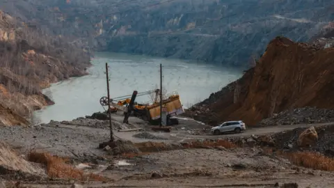 Getty Images Mining machinery and a car at the open-pit Zavallya mine, with mountains and a lake in the background