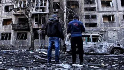 Getty Images Two men look at damaged apartment block in Dobropillya, Ukraine