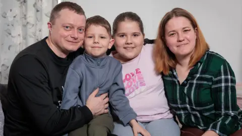 Andy Jones/BBC Ivan Vitsyn (left) and Olesia Aladko (right) smiling with their children Kyrylo and Oleksandra