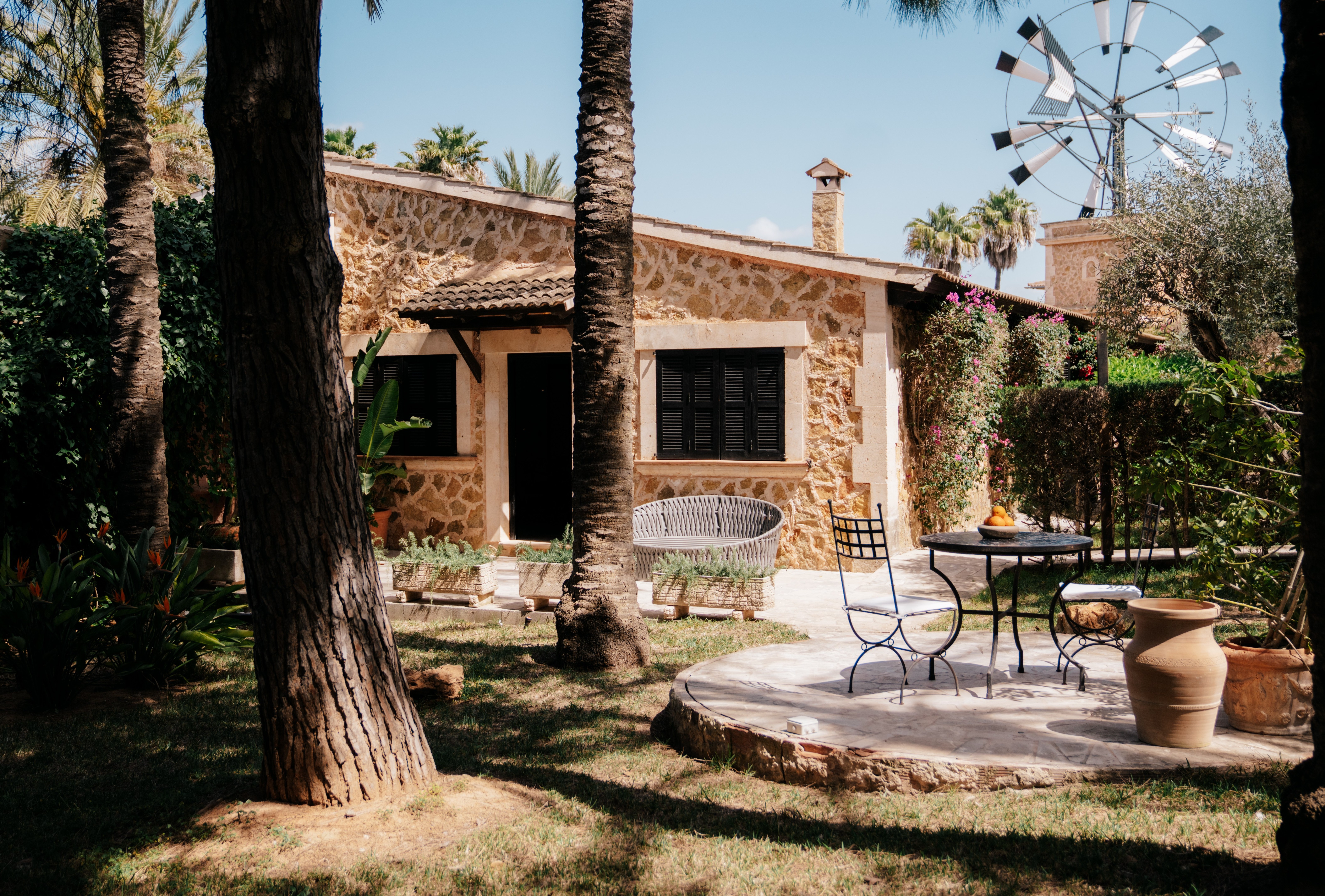 Stone country house with patio furniture and windmill in background.