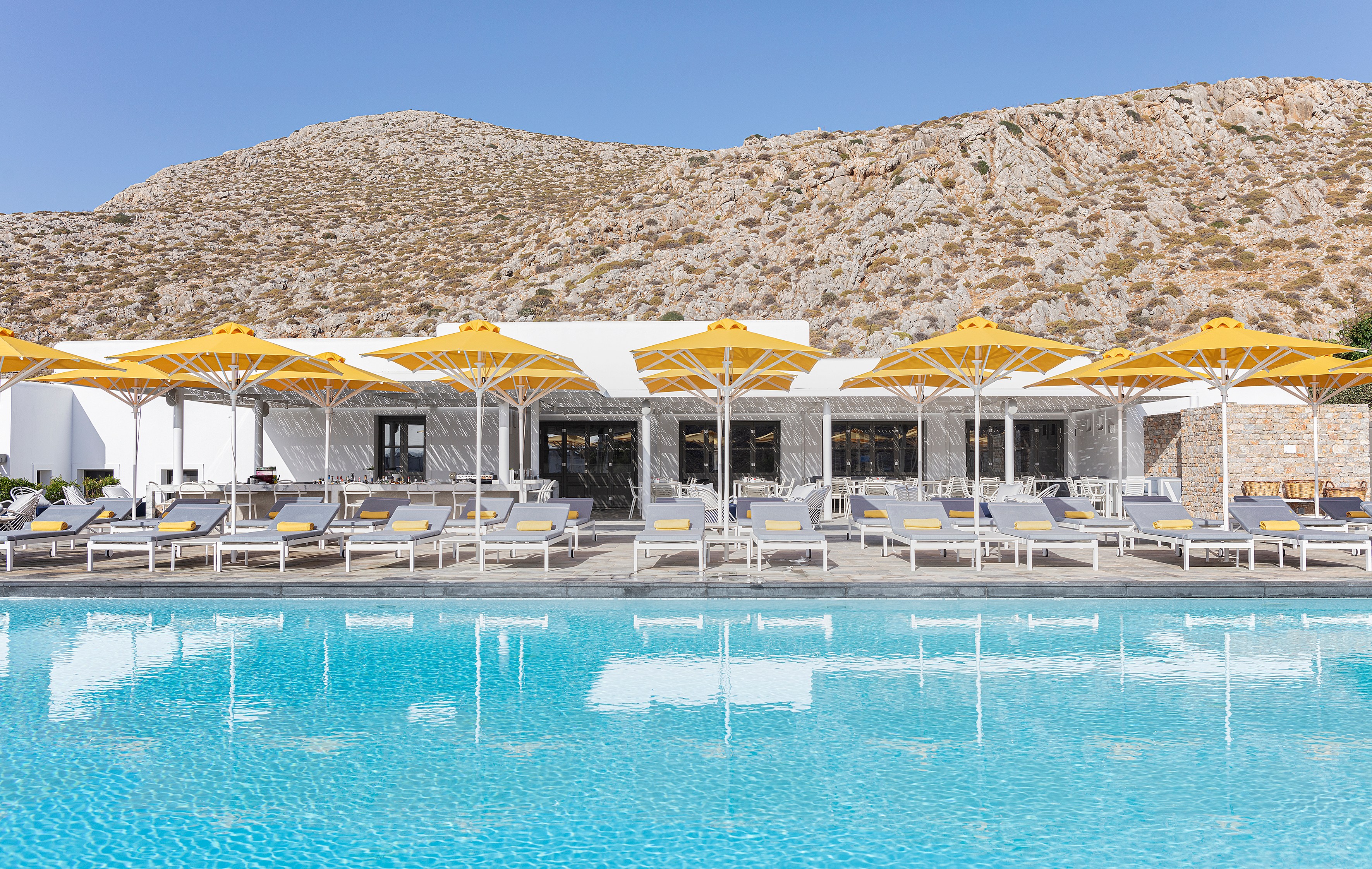 ANEMI Hotel & Spa Folegandros pool area with yellow umbrellas and lounge chairs.