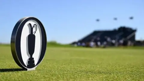 Getty An Open logo coin on the course of Royal Portrush. A blurred bandstand can be seen in the background.