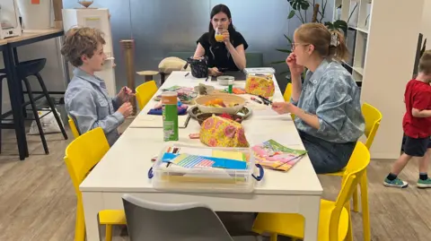 A group of three people sat at the end of a table talking and working on drawings and content for the magazine. They are sat on yellow chairs in an office.