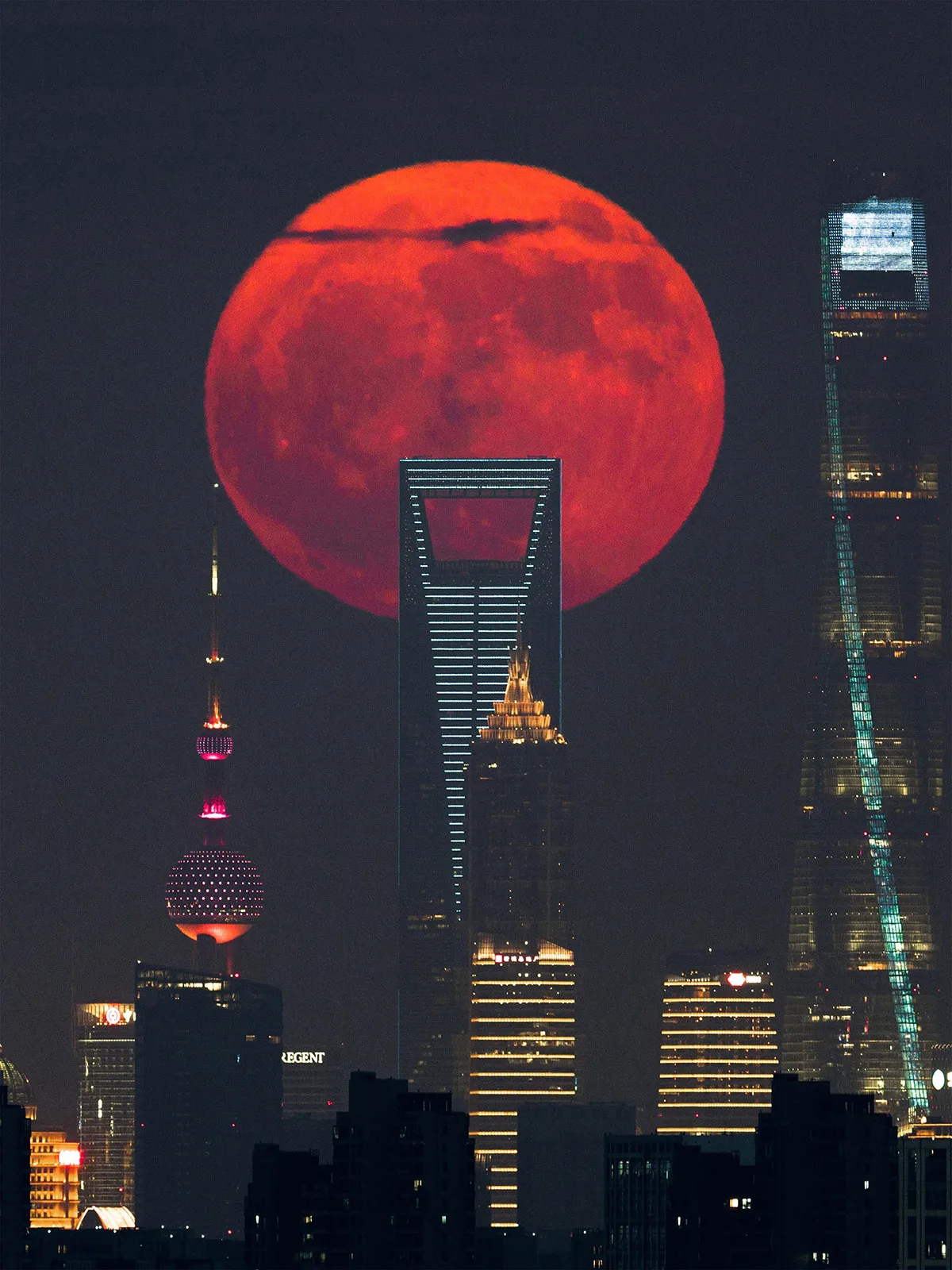 Blood Moon Rising Behind the City Skyscrapers © Tianyao Yang. Taken with a Sony ILCE-7RM4 camera, 600 mm f/4, ISO 250, 1/10-second exposure. Location: Jiading District, Shanghai, China, 21 July 2024