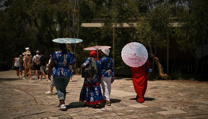 Tourists hold umbrellas as they walk in front of the closed Acropolis Hill in Athens, Greece, during a heatwave on July 8, 2025. — AFP