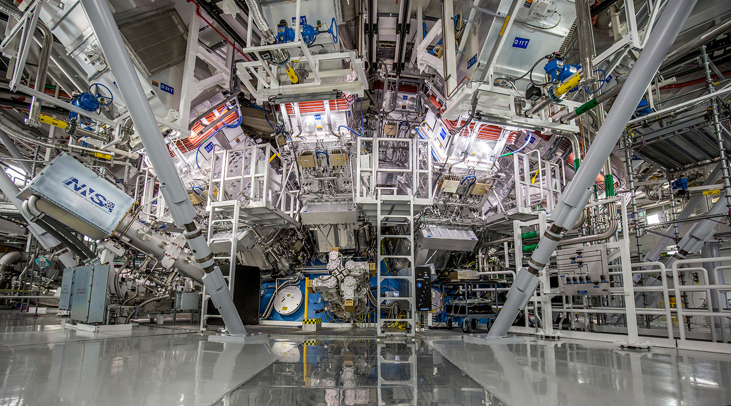 Interior view of the National Ignition Facility, showing an intricate array of equipment and support structures converging toward the center where experiments take place.