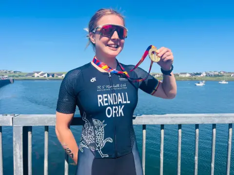 Claire Rendall holding her gold medal from the triathlon
