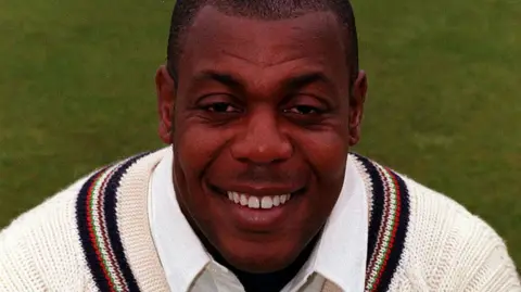 PA Media David 'Syd' Lawrence smiling at the camera wearing a thick cricket jumper