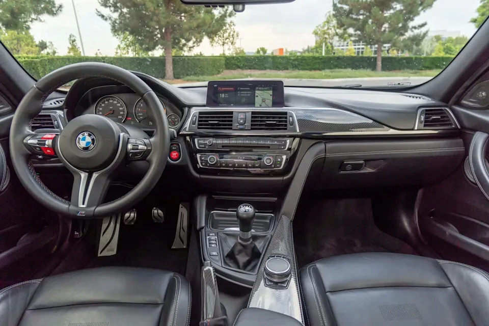 interior view of dashboard with analog gauges, center screen, manual gear shifter, and carbon trim.