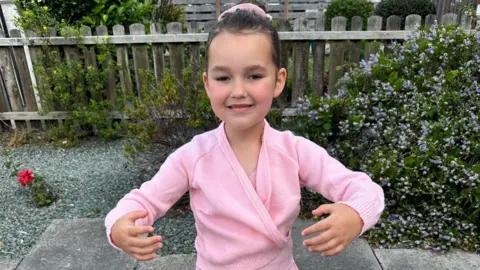 Family photo Image shows Bebe King wearing a pink ballet costume and standing in a ballet pose in a garden. 