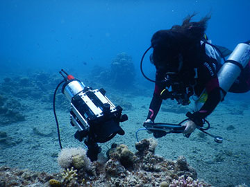 Scuba diver with large device over coral
