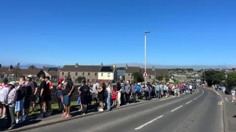 A queue of people standing down the side of a road