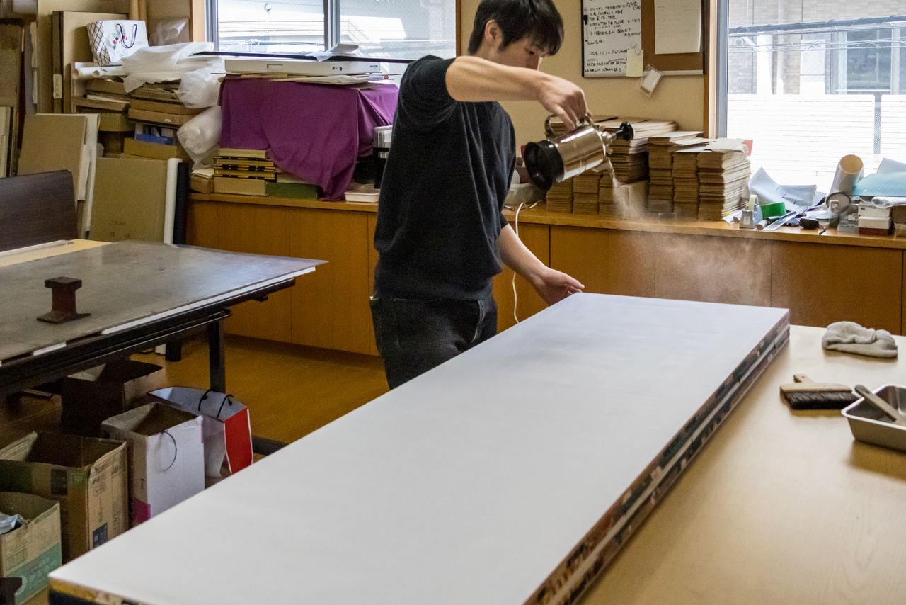 An artisan at Kataoka Byōbu uses a traditional technique to smooth the surface of the folding screen in preparation for printing. (© Nippon.com)