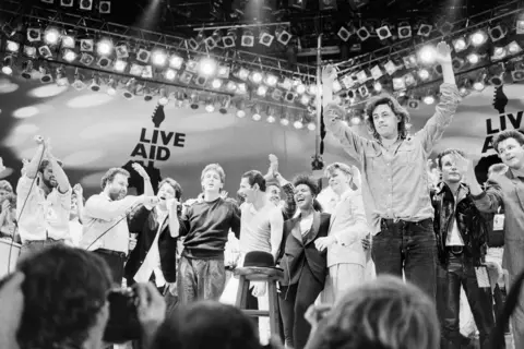Getty Images Black and white photo of various stars who performed at Live Aid on the stage including Bono, Paul McCartney, Freddie Mercury, David Bowie and Bob Geldof