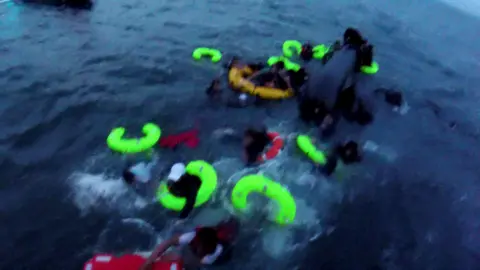 BBC Yellow and red life-bands in the sea as people try and cling on to them. The picture is slightly blurry as it has been taken from a bodyworn camera.