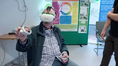 BBC Stuart Spray wearing a virtual reality headset and holding two hand controllers