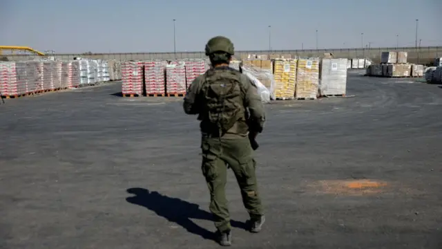 An Israeli soldier stands next to the parcels of humanitarian aid awaiting to be transferred into Gaza from Israel,