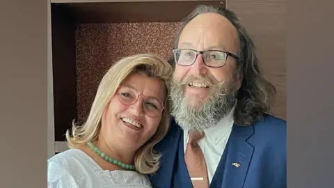Family handout Lili and Dave Myers have their arms around each other and are smiling at the camera. Lili has mid-length blonde hair and is wearing a white top. Dave has mid-length brown hair and a grey beard. He is wearing a blue suit.