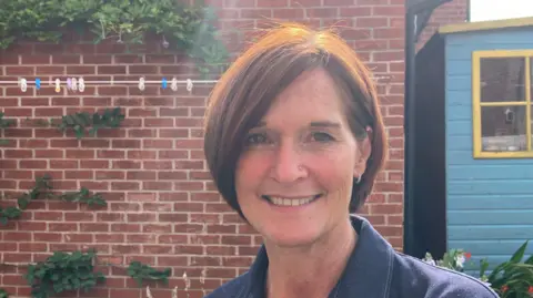 A woman with a brown bob and a blue top, sitting in the garden of her new home