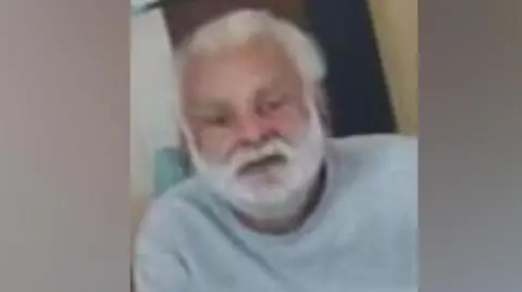 Bedfordshire Police Sukhjinder Singh-Gill: A man with white hair and and white beard wearing a pale grey, round-necked. long-sleeved, top.