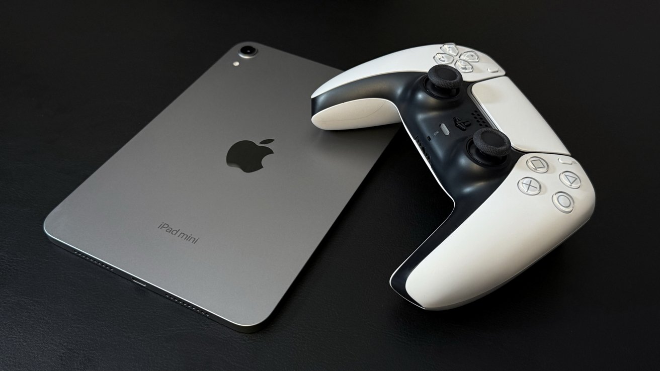 A silver iPad Mini lies on a black surface next to a white and black video game controller.