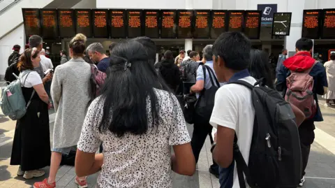 BBC A crowd stands in front of a row of screens that should show train departure times but all say "Special Notice" on them.