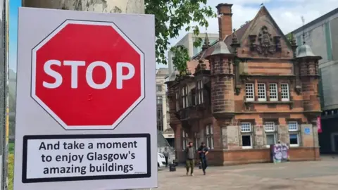 @ASignOfHumour A photo of the former St Enoch station in the centre of Glasgow and a sign which says STOP - and take a moment to enjoy Glasgow's amazing buildings