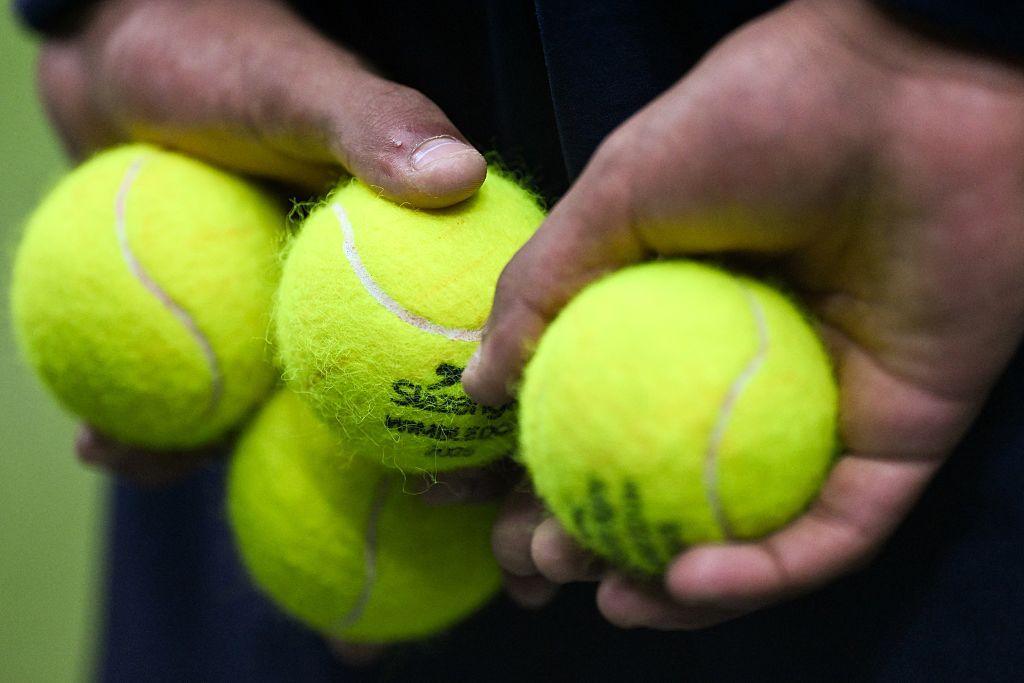 A member of the ball crew holds four tennis balls in their hands behind their back at Wimbledon in 2025.