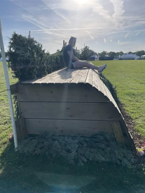 Margaret Kane A young woman sits on a large wooden cross-country eventing obstacle