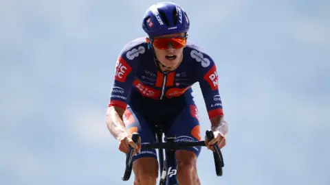 Reuters Cyclist Oscar Onley in blue and orange kit with a blue helmet and orange reflective sunglasses