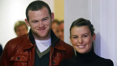 PA Media Wayne and Coleen Rooney standing next to each other and both smiling on a visit to Alder Hey Children's Hospital in 2006