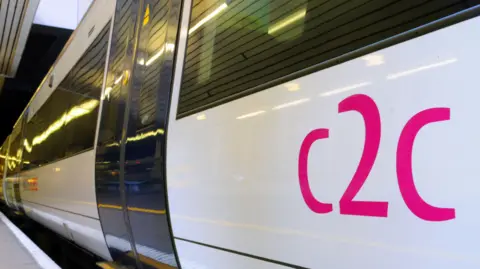 c2c A white train with c2c printed on the side in pink. The train is parked next to a platform.