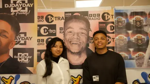 BBC A teenage girl with long black hair wearing a white shirt next to a man with short black hair and a black t shirt.