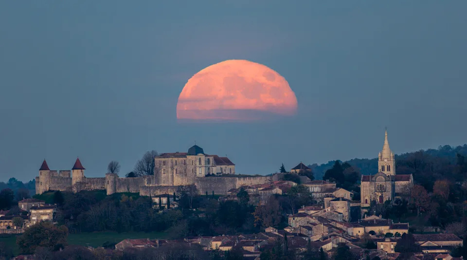 half of the pink moon above an ancient city