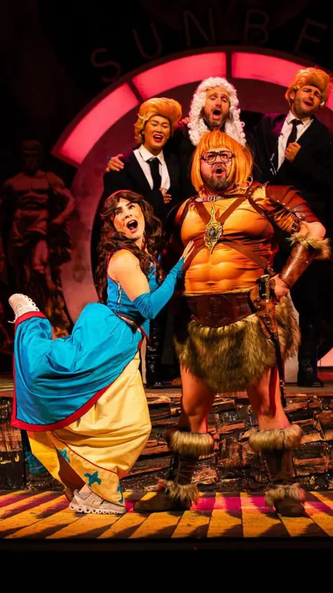 Andrew AB Photography Stage photograph of actors in medieval clothes playing Coleen and Wayne Rooney, with three actors in suits and judges' wigs behind them