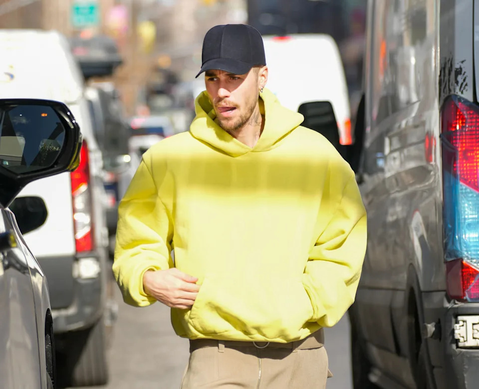 A person in a casual hoodie and cap walks on a busy street, flanked by vehicles