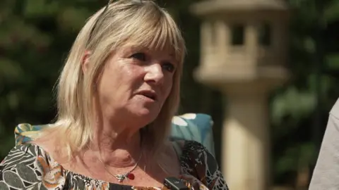 Eileen Punter, wearing a floral top, sitting in a garden in sunshine