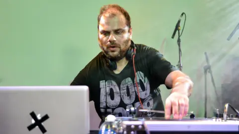 Getty Images A man DJing behind decks - he has a beard and thin hair 