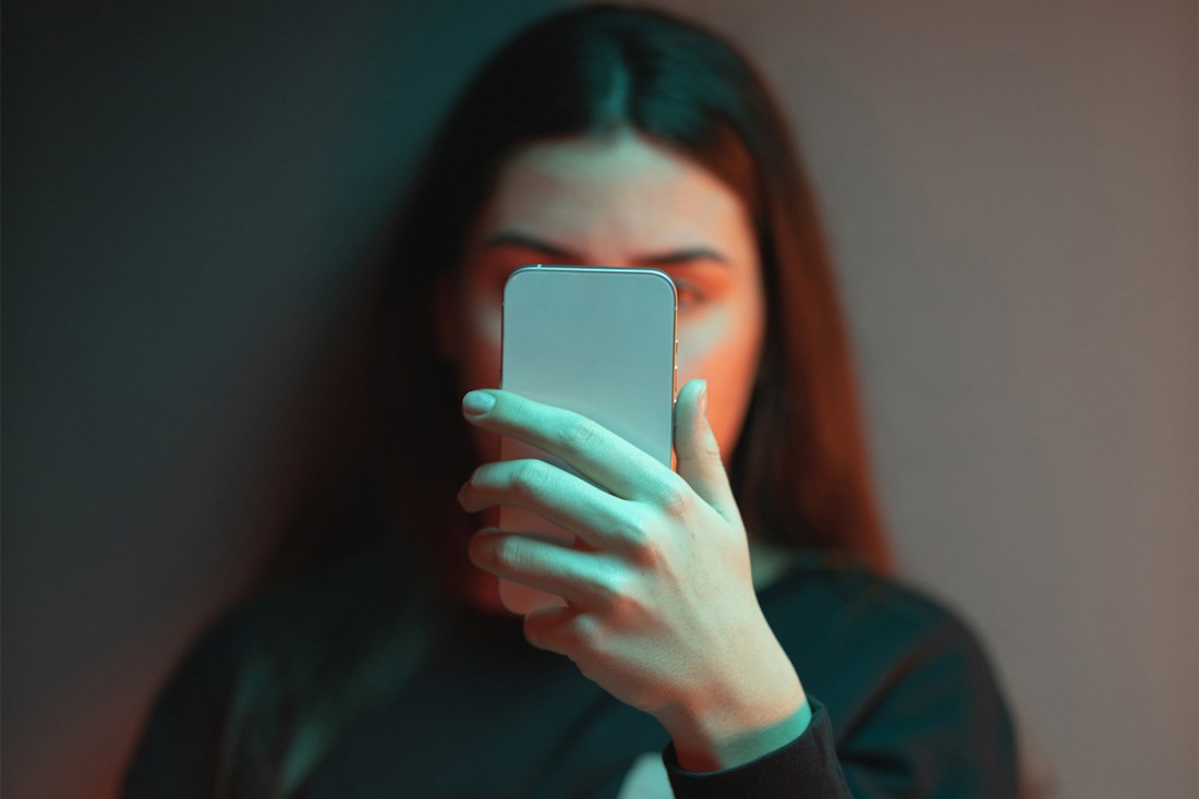 Person holding smartphone with a blue screen light illuminating their face in a dimly lit room.