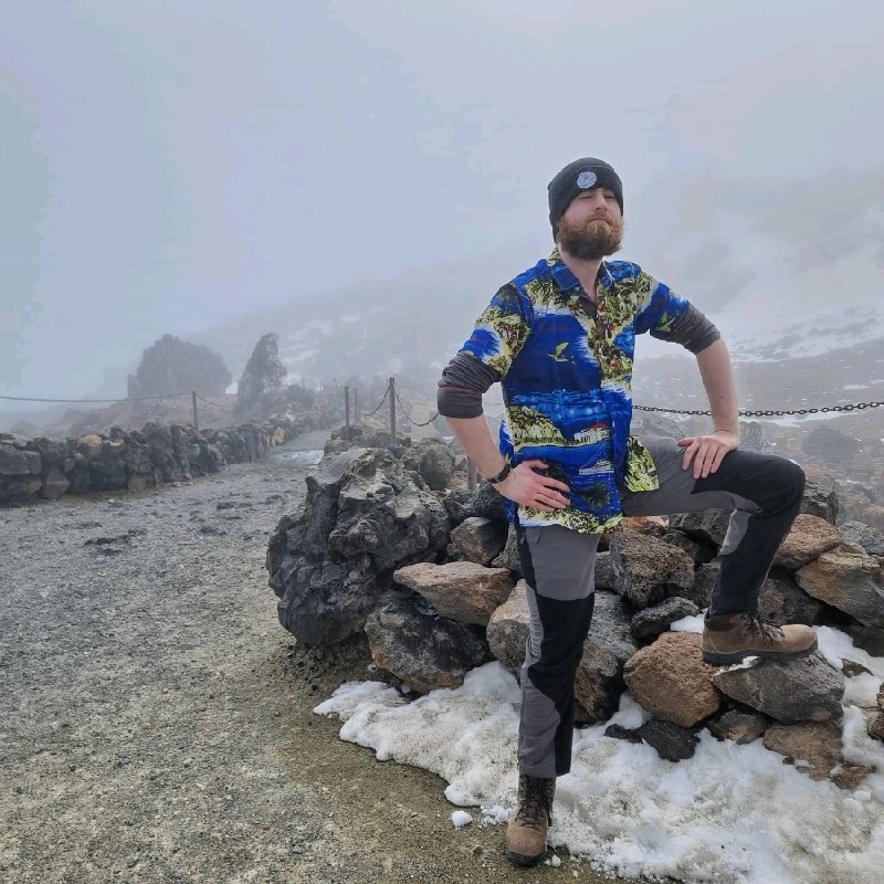Man with beard and toque posing on a collection of rocks with some snow on the ground.