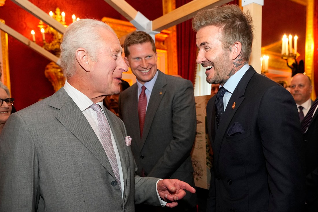 David Beckham greeting King Charles III with a laugh while King Charles III is in the middle of saying something.