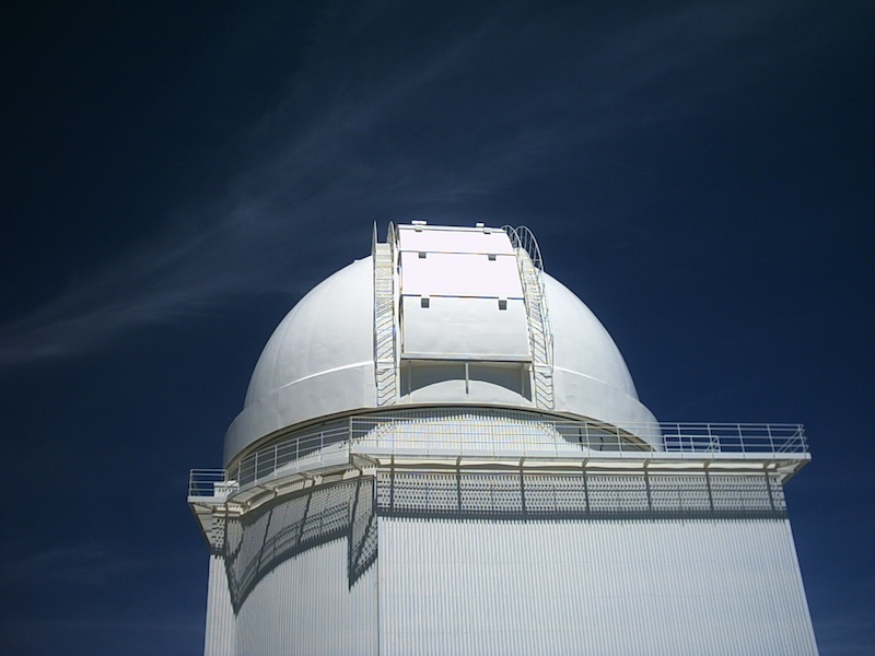 White telescope observatory dome with walkway around it. The sky above is deep blue with wispy cirrus clouds.