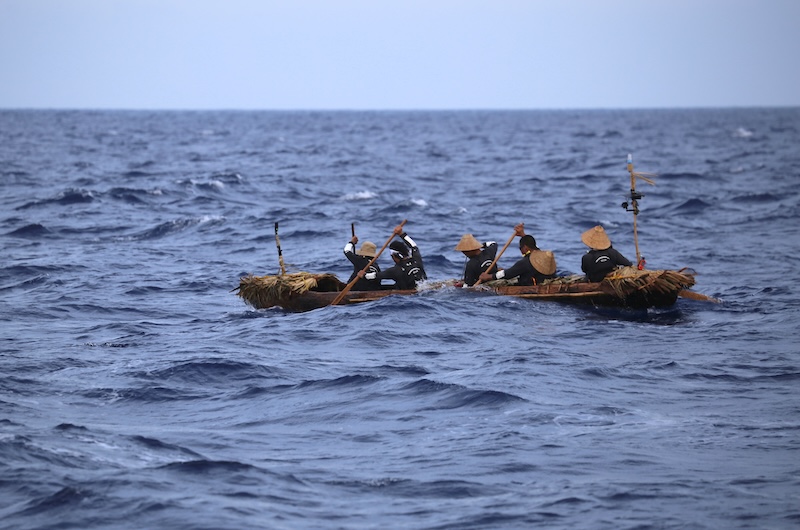 Five people in a canoe in choppy ocean waters