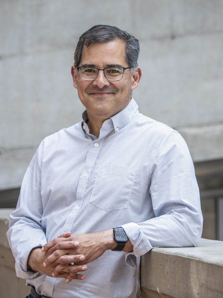 smiling man with glasses leaning against a concrete railing