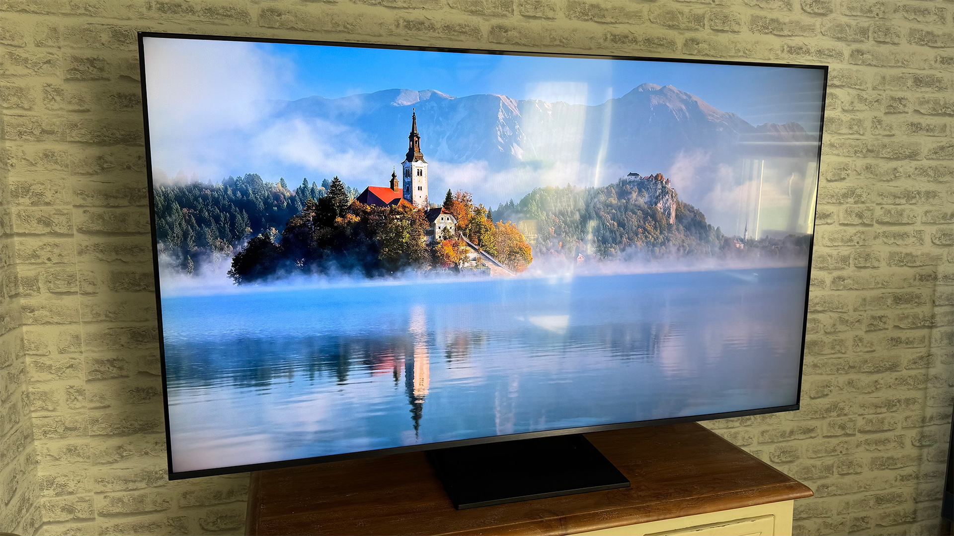 LG 65QNED93 LCD TV against brick wall, on screen is lake scene with church reflected