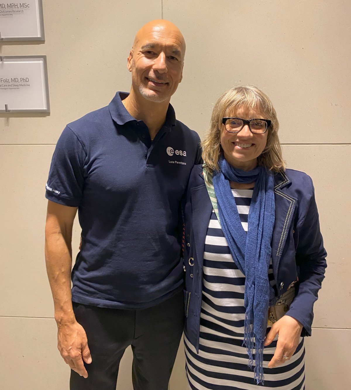 A tall man in an ESA t-shirt and a woman in a stripy dress stand next to each other smiling in a hallway.
