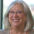 Lisa Coussens, Ph.D., has shoulder-length blonde hair, eyeglasses, and a beige sweater, smiling.
