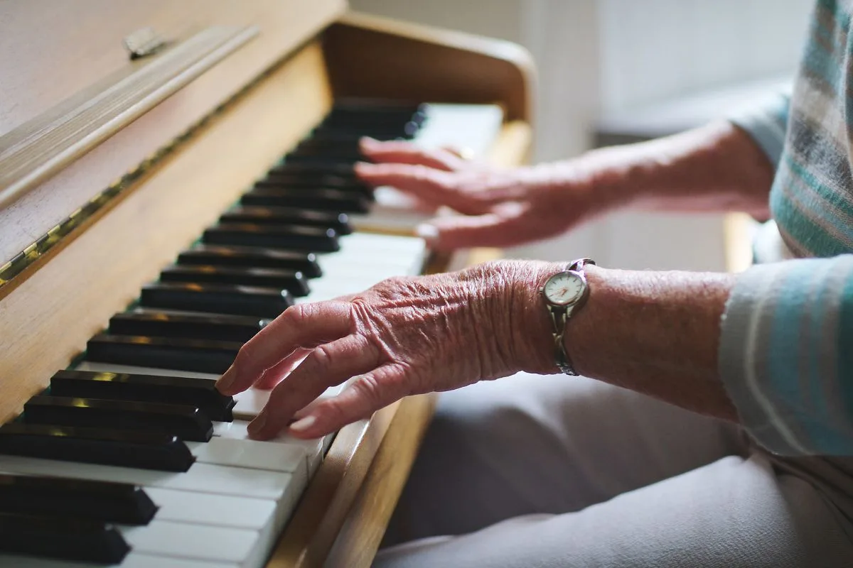 Old hands play the piano, wearing a small watch.