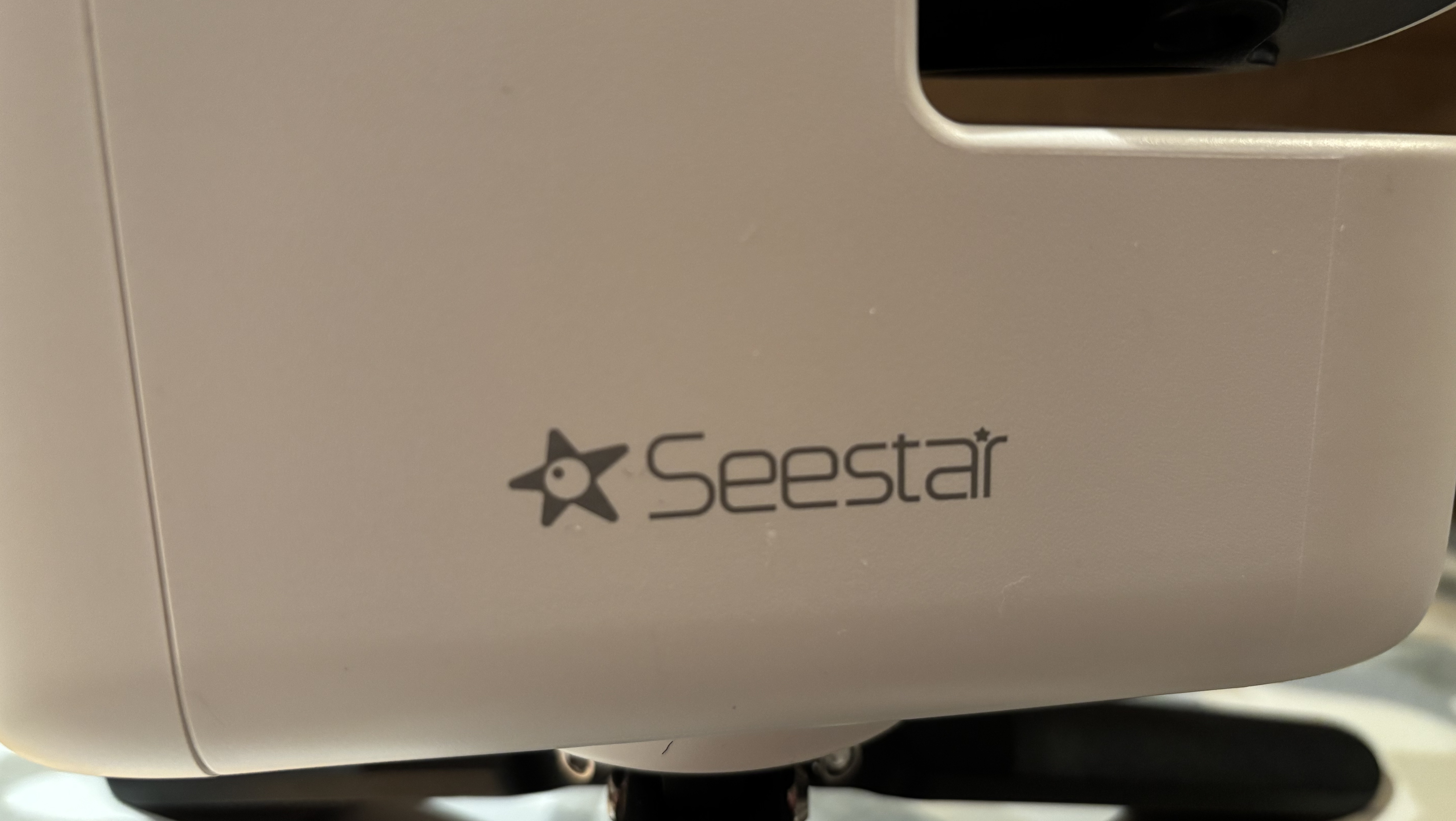 A close up of the Seestar logo on a white telescope - the logo is a dark star with a white circle in the centre and the word 