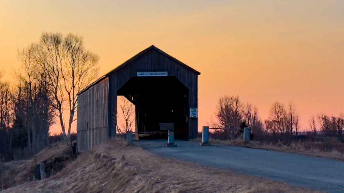 A covered bridge next to a road is captured at sunset in Canada